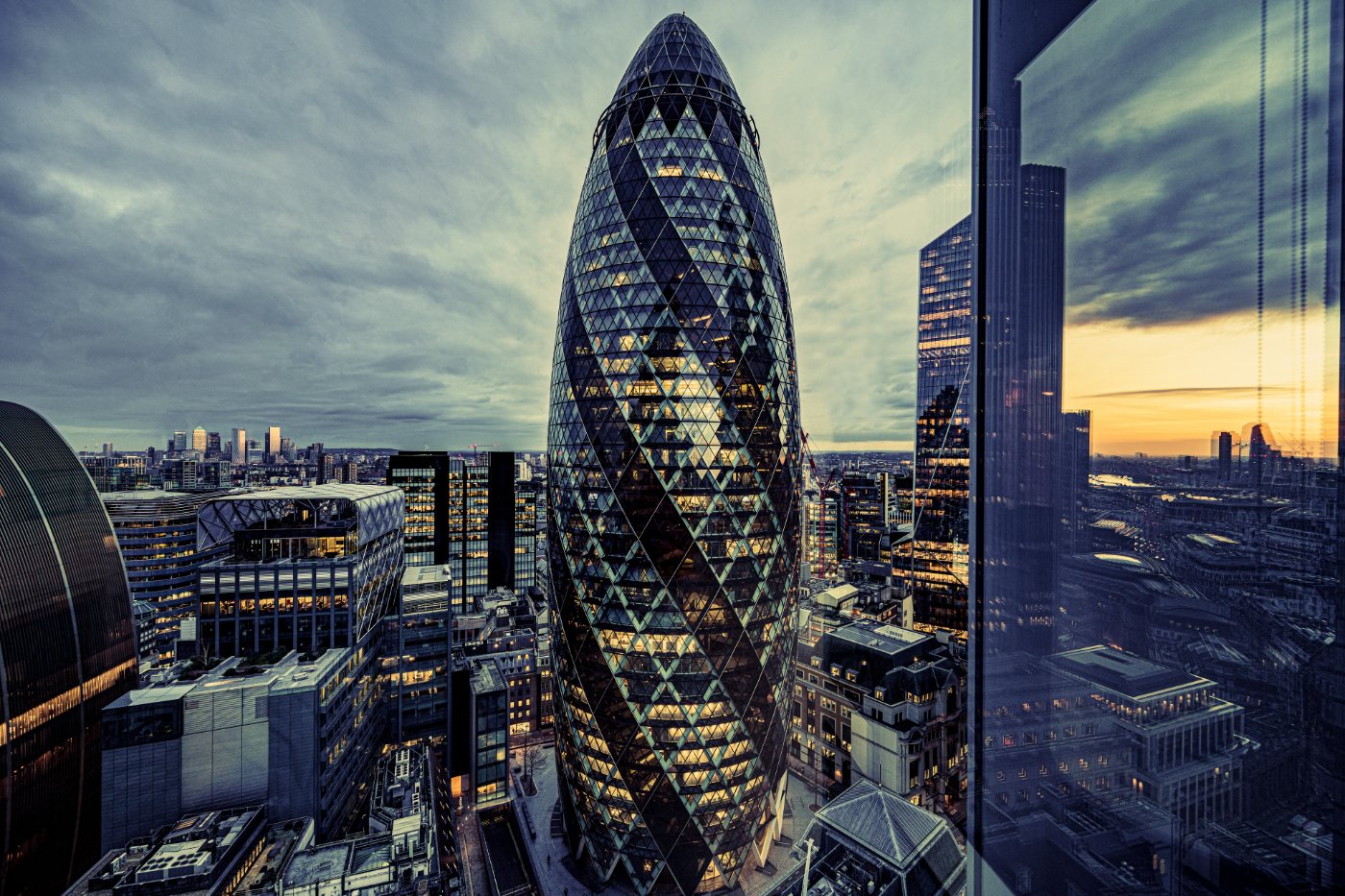 30 St Mary Axe (The Gherkin) sett fra høyden, med solnedgangslys reflektert i glassfasaden under cirrusskyer.