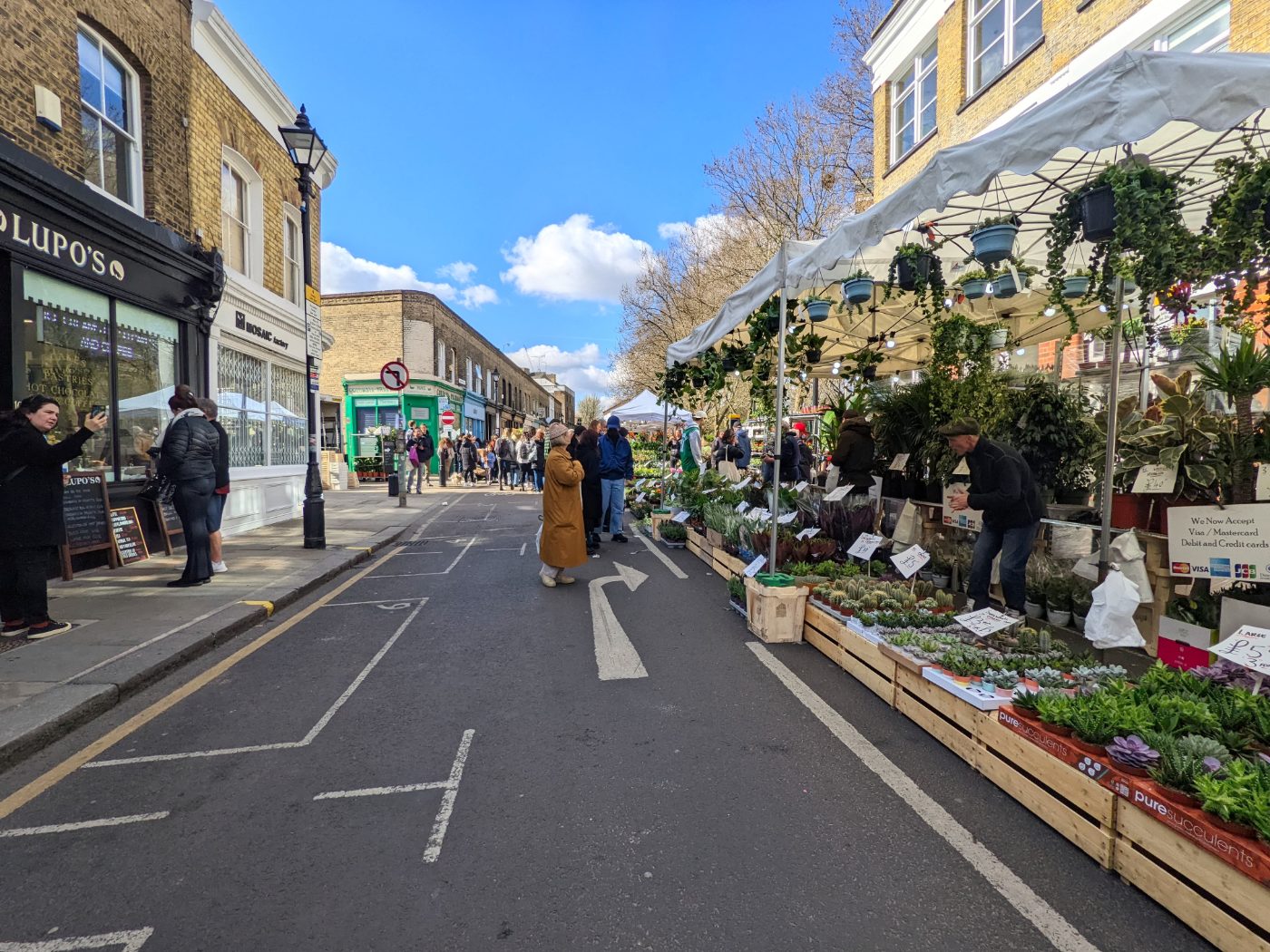 Livlig scene på det kjente Columbia Road Flower Market i London, med folkemengder og boder fulle av planter.