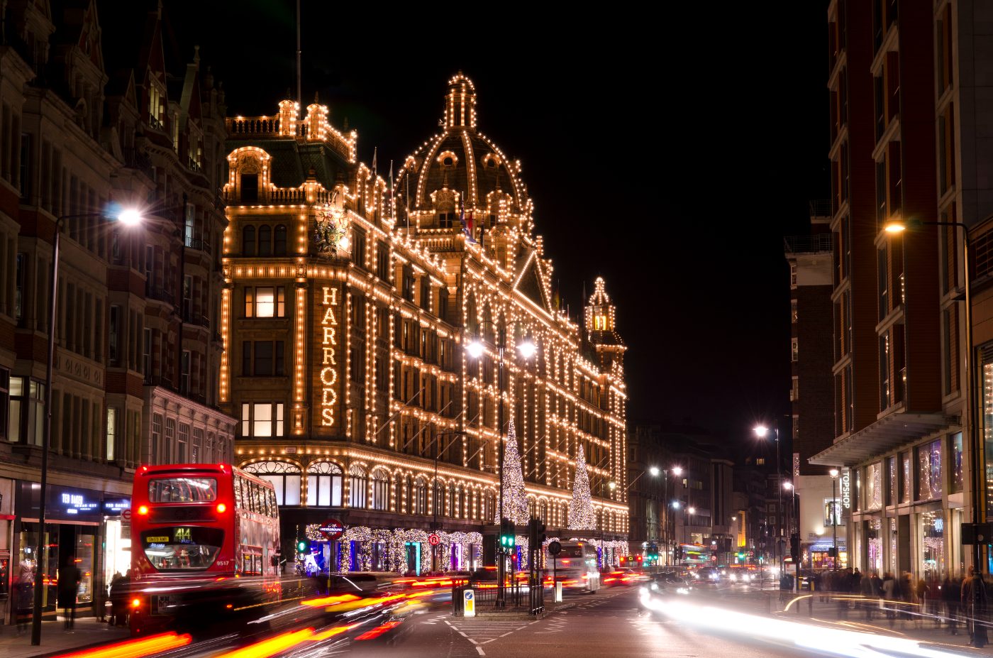 Harrods varehus i Knightsbridge på Brompton Road, dekorert til jul, med trafikk og kveldsshoppere utenfor.