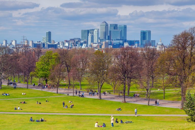 Folk som slapper av i Greenwich Park, med skyskraperne i Canary Wharf i bakgrunnen.