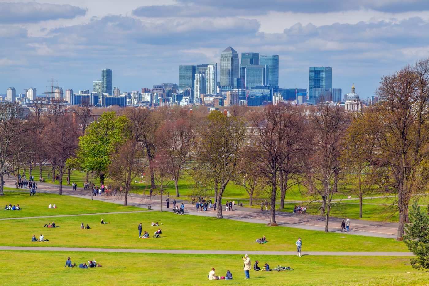 Folk som slapper av i Greenwich Park, med skyskraperne i Canary Wharf i bakgrunnen.