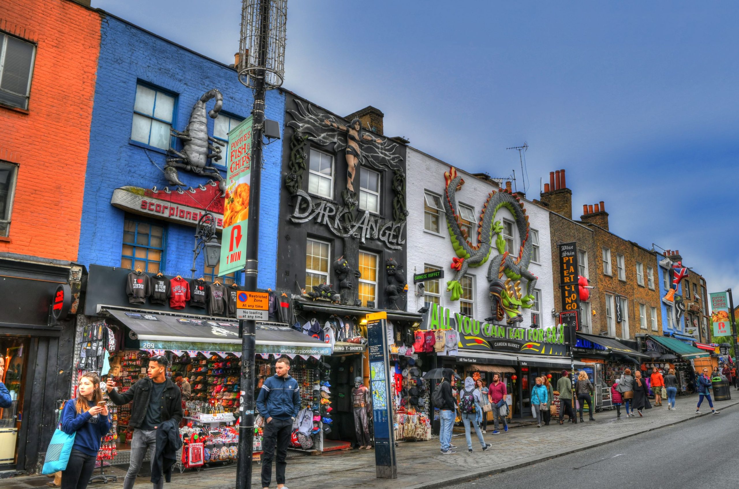 Turister som går forbi fargerike hus og butikker i Camden Town under blå himmel i London, Storbritannia.